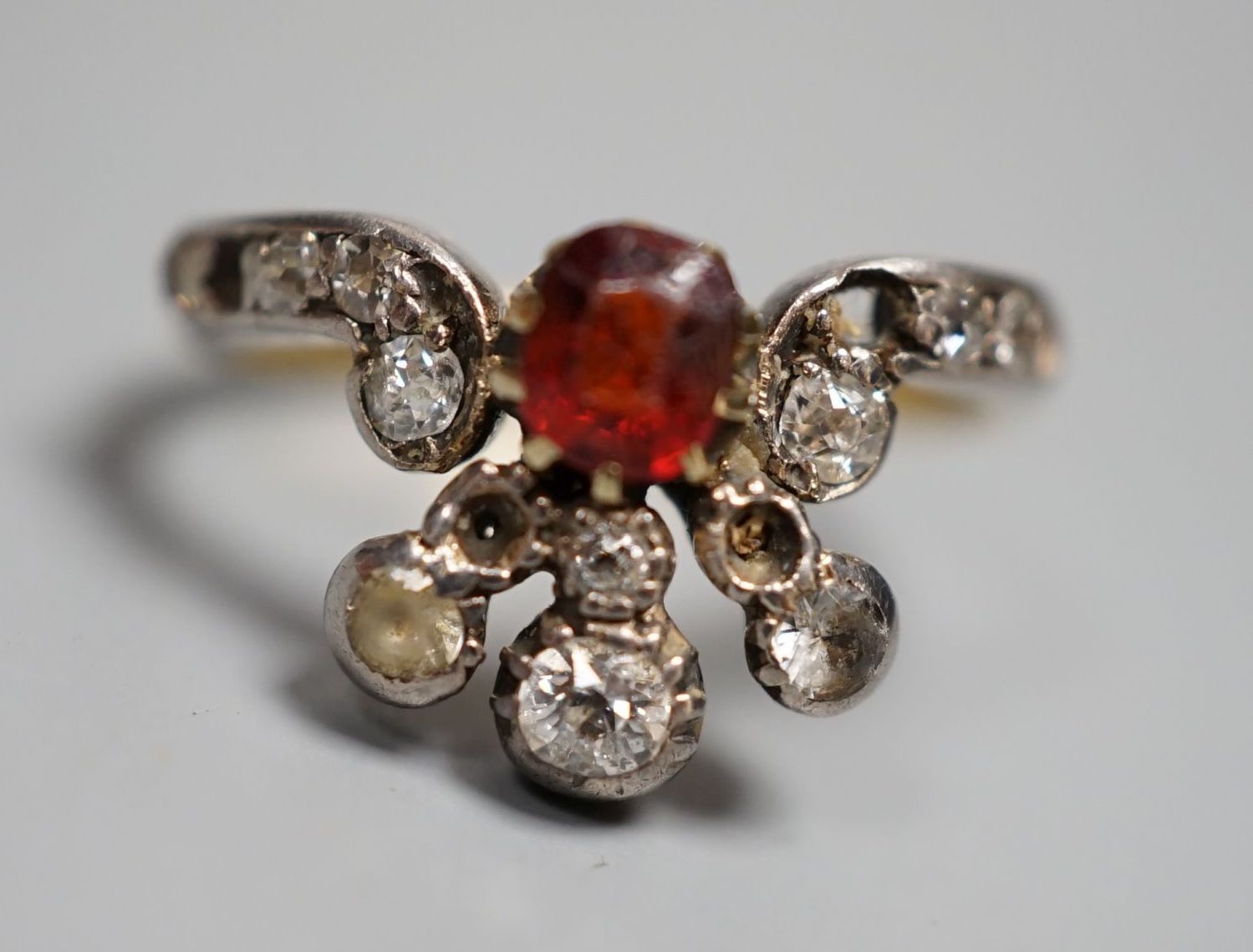 An early 20th century 18ct, garnet? and diamond cluster set dress ring(a.f.), with diamond set shoulders, size J. gross weight 3.5 grams.